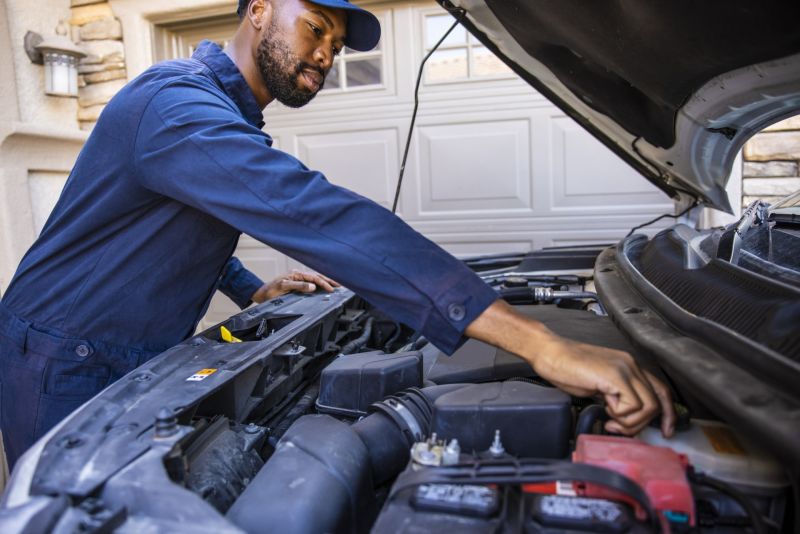 Mechanic checking engine under car hood in a driveway during an oil change service